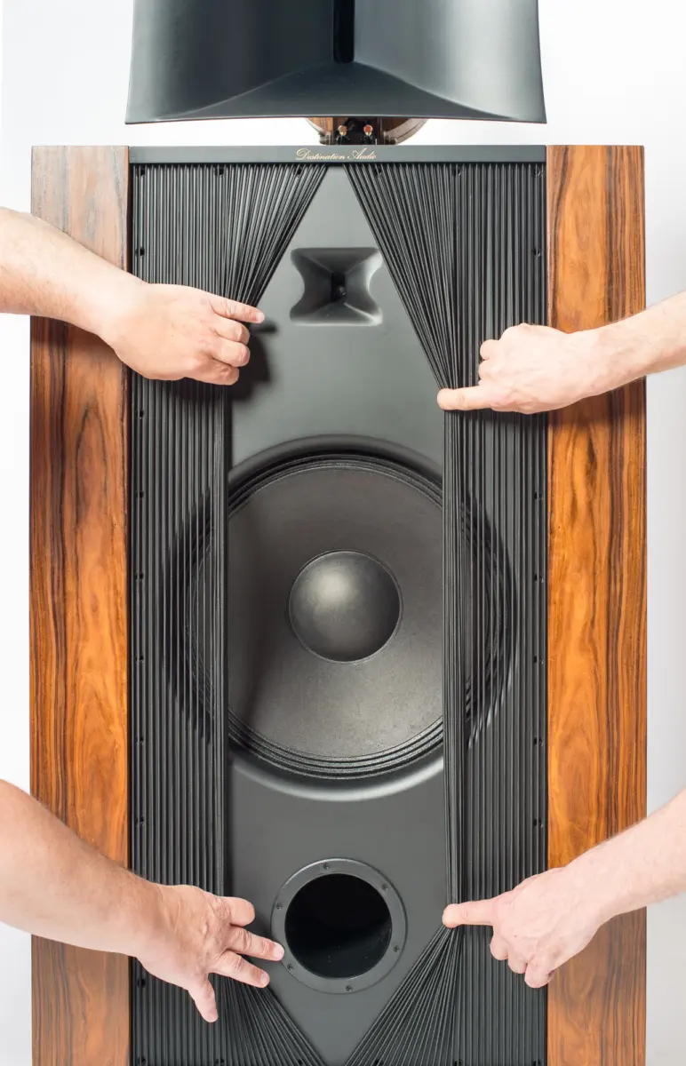 Four hands pulling the grille aside on a Destination Audio Nika to show its large woofer and port