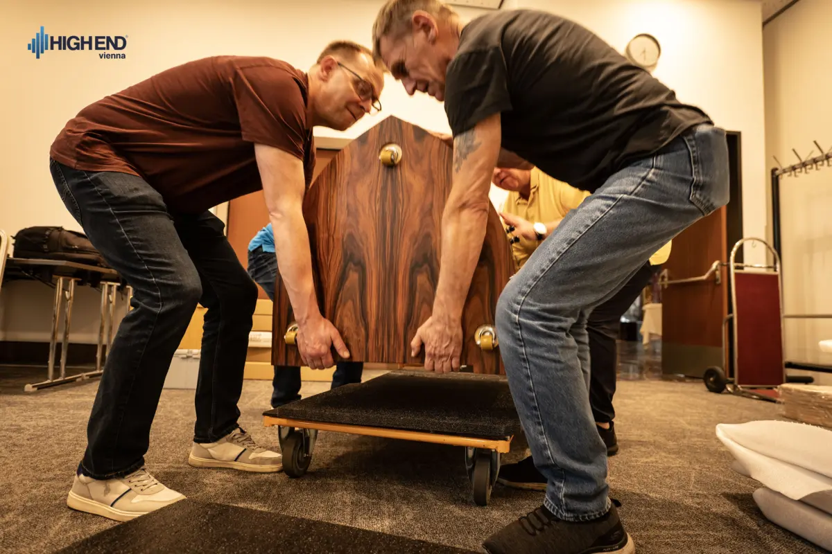 Two men lifting a rosewood Destination Audio speaker cabinet onto a moving dolly
