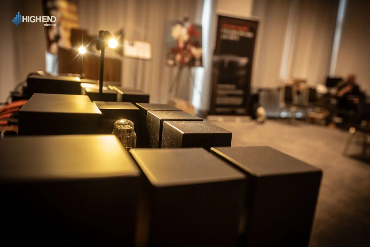 Black transformer housings and a tube of a Destination Audio amplifier, with the show room blurred behind