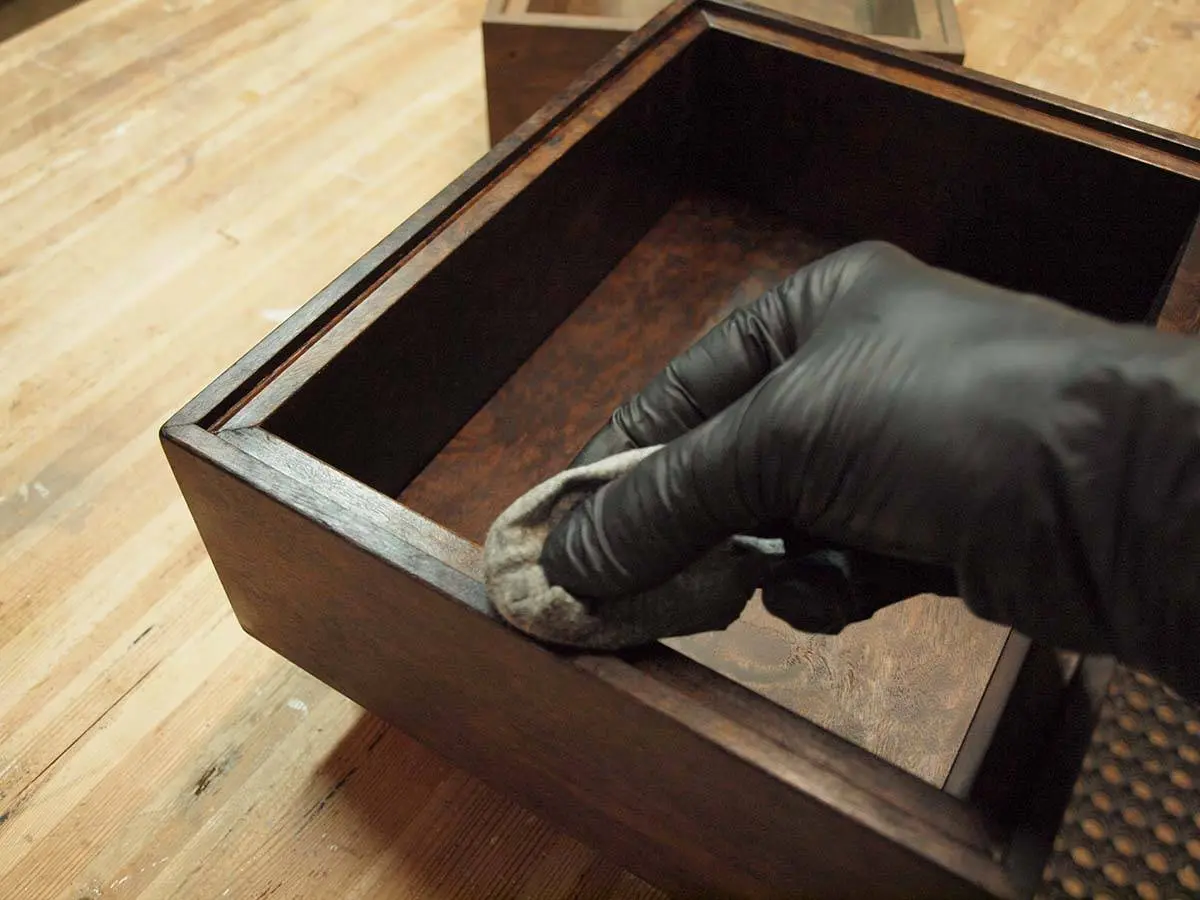 A gloved hand polishing the inside of a walnut wooden box