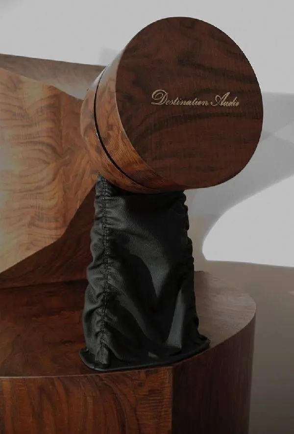 Round walnut driver housing engraved Destination Audio, resting on a black leather sleeve