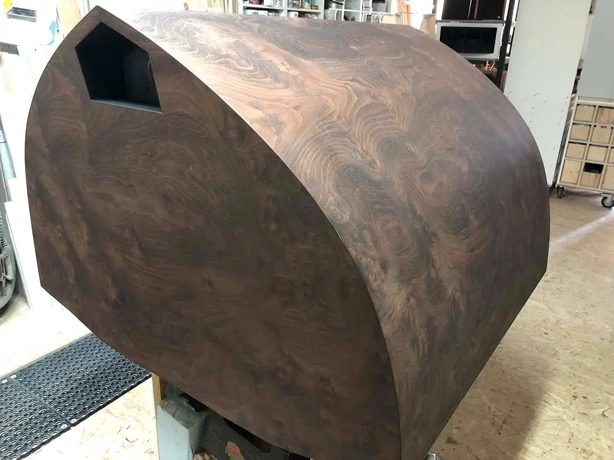 A curved burl walnut speaker cabinet with an opening for the horn, in the workshop
