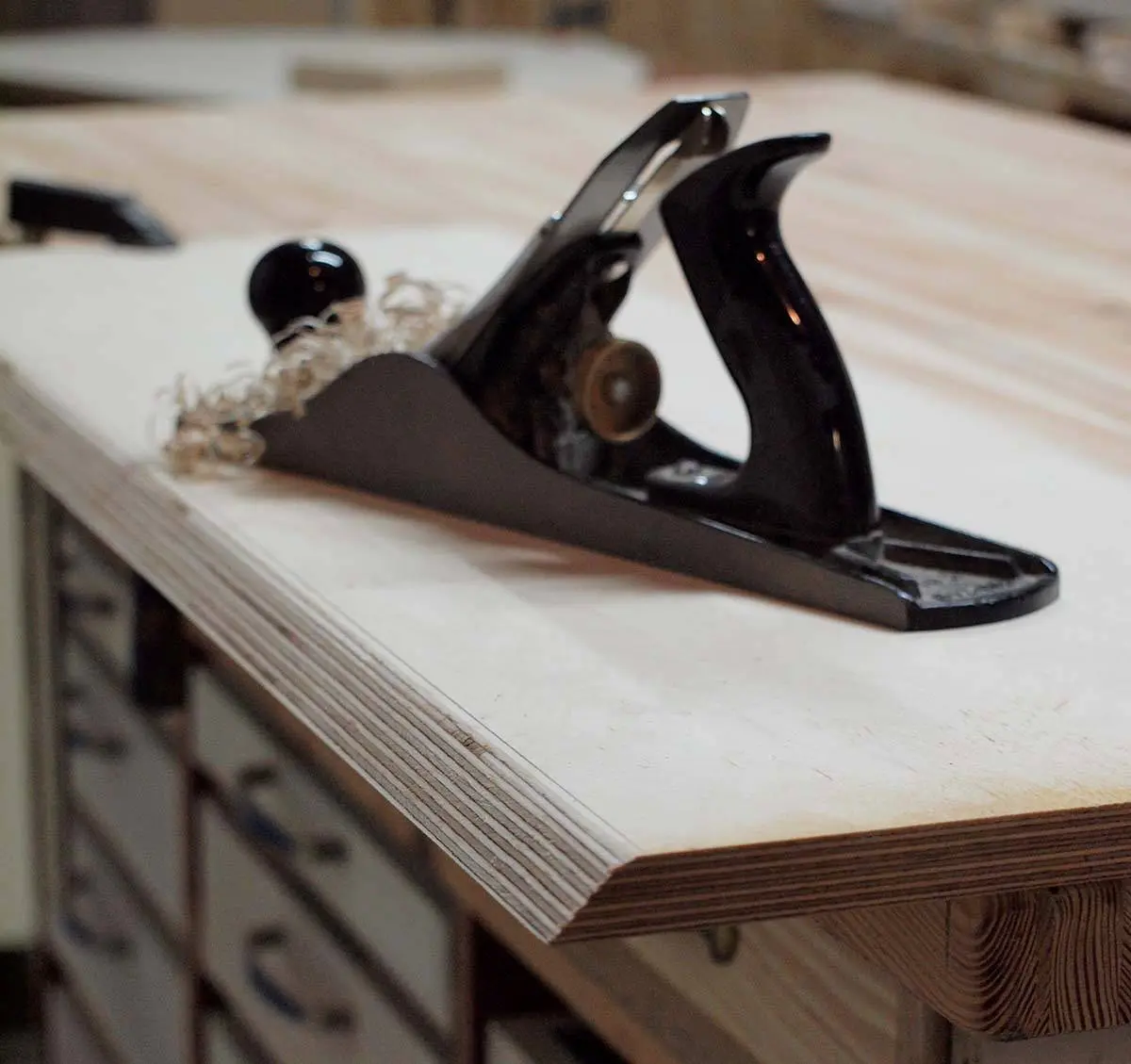 A hand plane with wood shavings on the edge of a plywood panel on a workbench