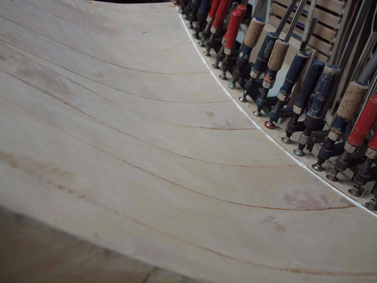 A curved glued wood panel held by a row of clamps